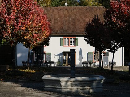Eingangsbereich zum Liliental mit zentralem Brunnen, Gasthaus, gesäumt von Herbstbäumen
